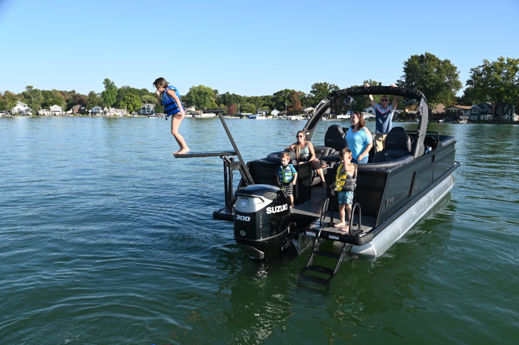 Child getting ready to jump from LilliPad Diving Board off Viaggio Pontoon Boat with family on board.