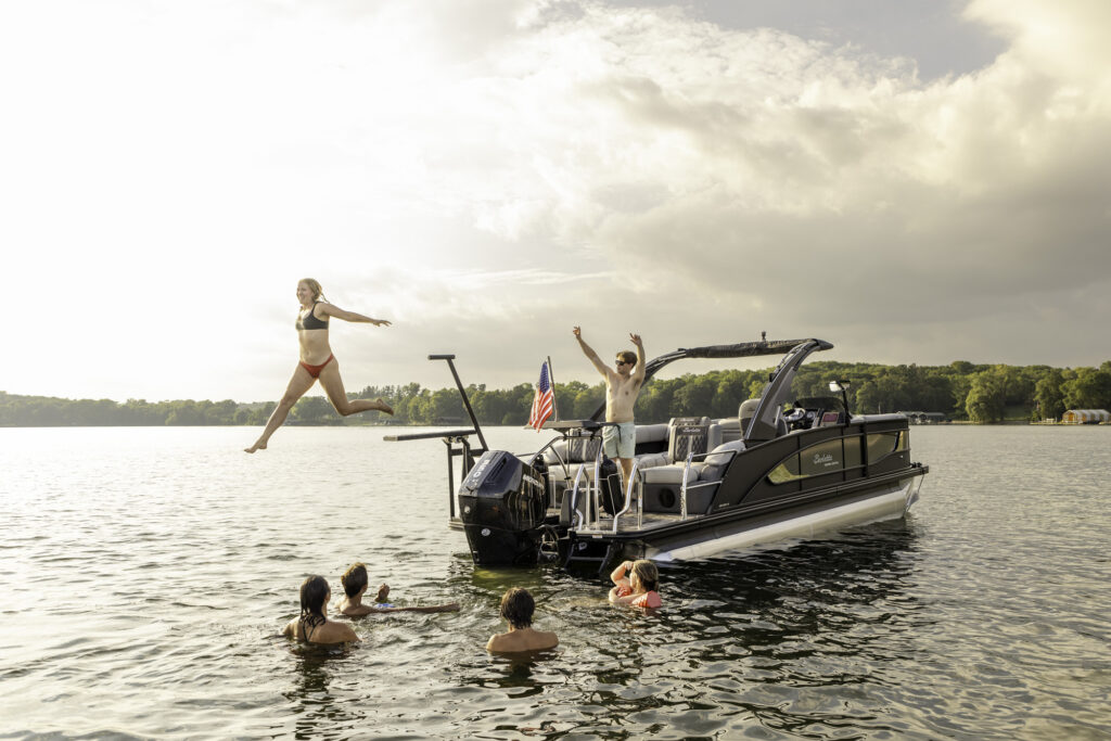 Girl jumping off LilliPad Diving Board from Barletta Pontoon Boat while being cheered on by a friend on the boat